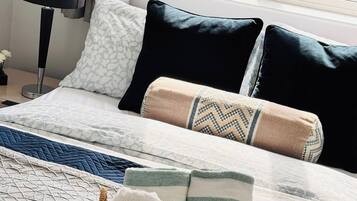 A neatly made bed with patterned bedding, a bedside lamp, and a basket of folded towels.