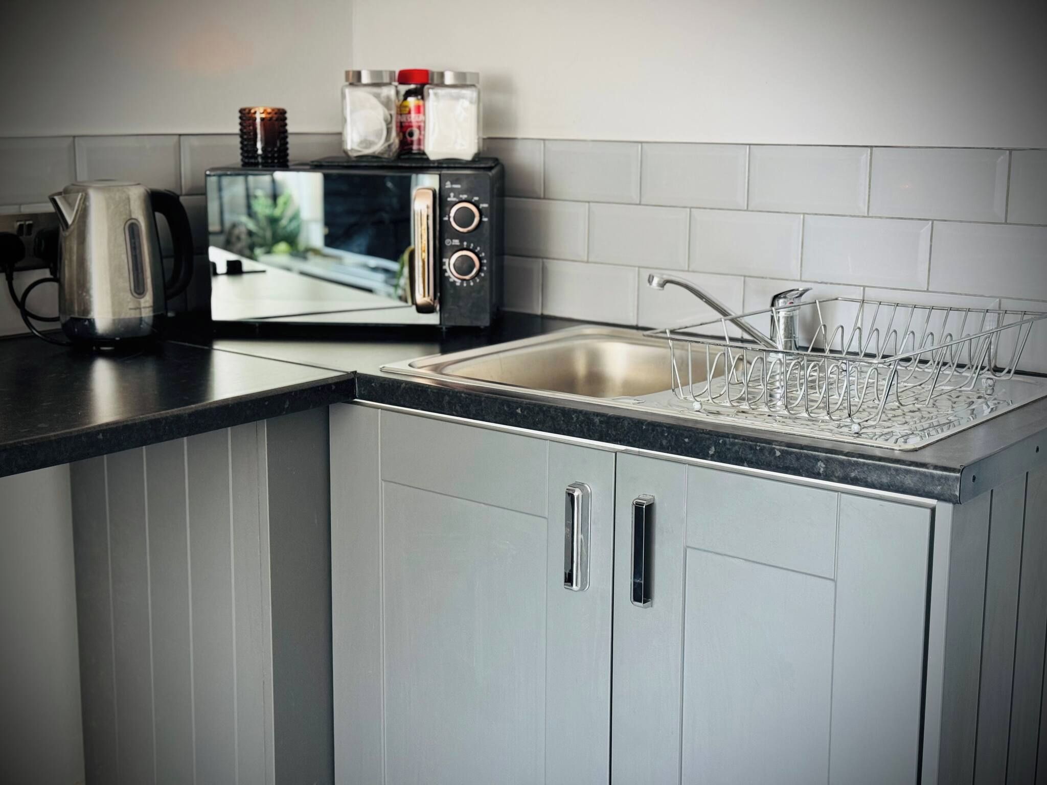 A kitchen with a built-in microwave, a kettle, and a dish rack.