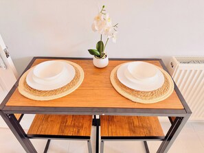 A rectangular dining table with two white plates and woven placemats, a potted orchid, and a radiator in the background. - Shal Inn at Heathrow free parking and ride on request (Berkshire)