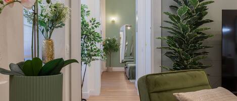 Un pasillo con piso de madera, una silla verde y plantas en macetas.