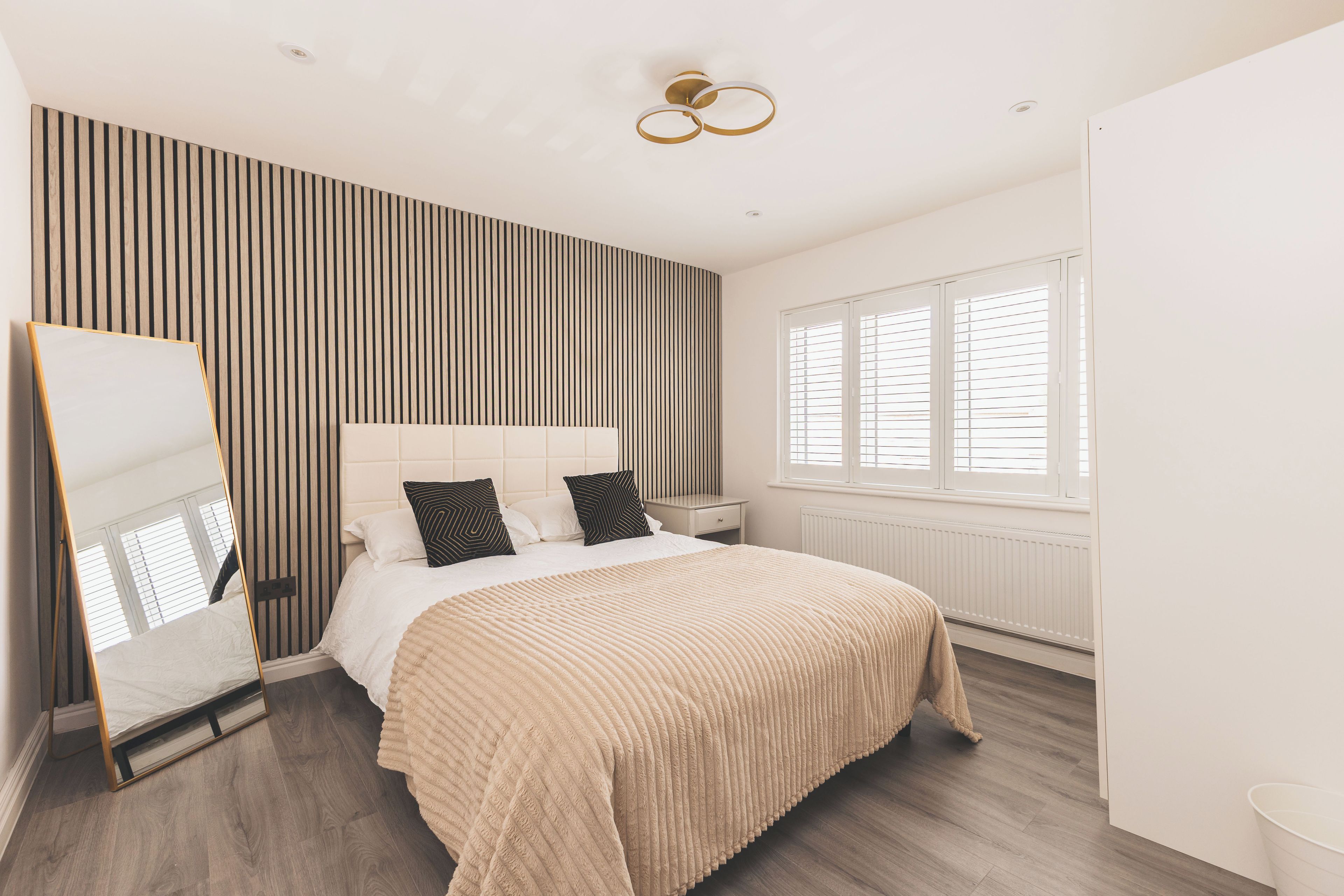 A modern bedroom with a bed, bedside tables, a mirror, and a window with blinds.