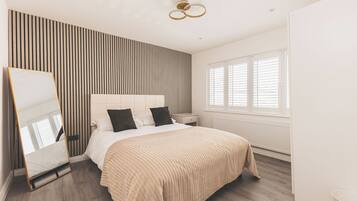 A modern bedroom with a bed, bedside tables, a mirror, and a window with blinds.