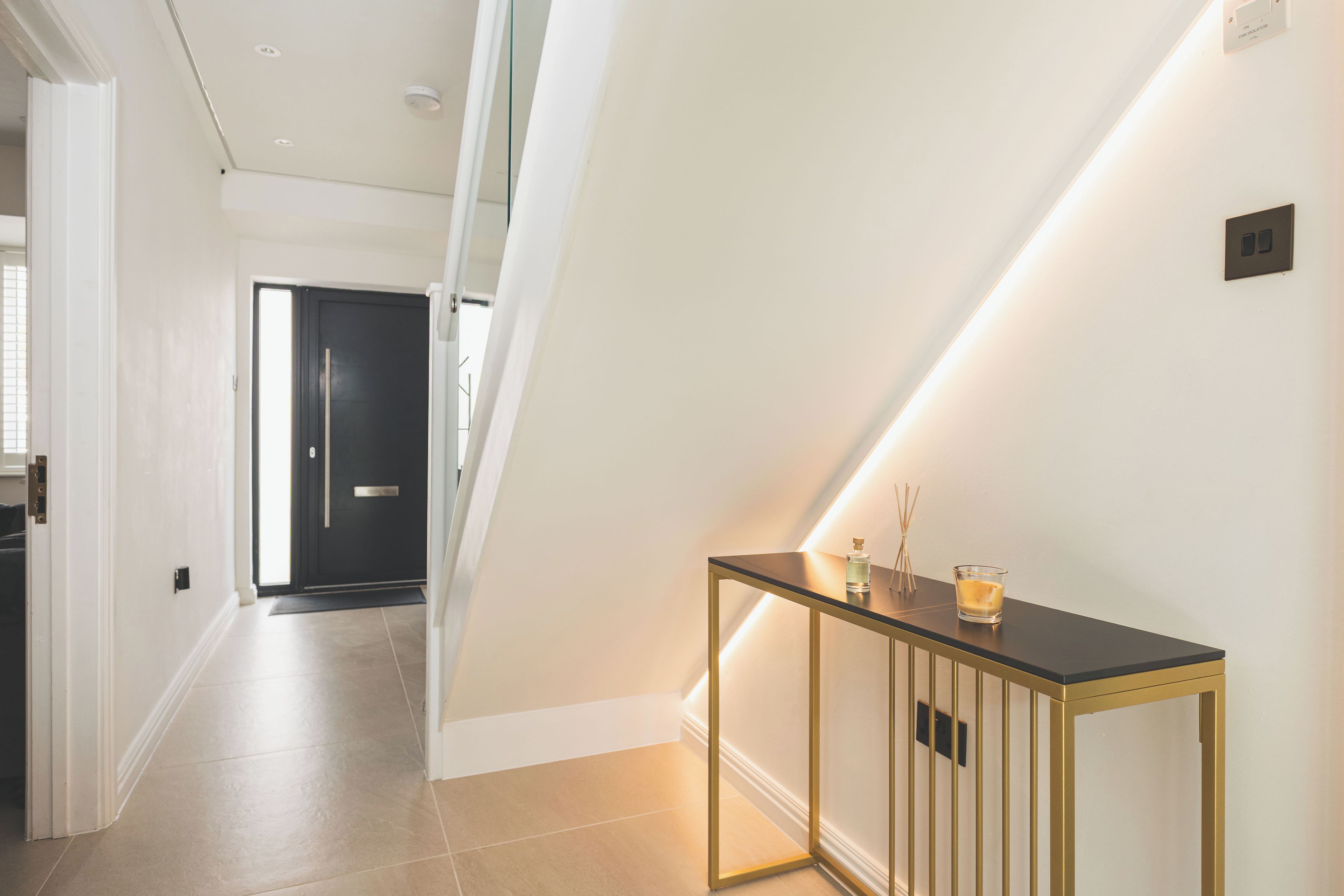 A modern interior with a glass door leading to a dark room, a console table with a candle, and a light strip on the wall.