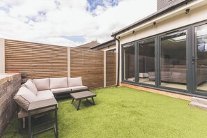 A patio with a sofa, a table, and a wooden fence. - Luxury 5BR Home | Office, AC & Parking | Heathrow (London)