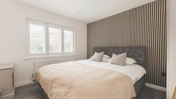 A bedroom with a bed, a radiator, a window, and a wall with vertical lines.