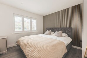 Ein Schlafzimmer mit einem Bett, einem Heizkörper, einem Fenster und einer Wand mit vertikalen Linien.