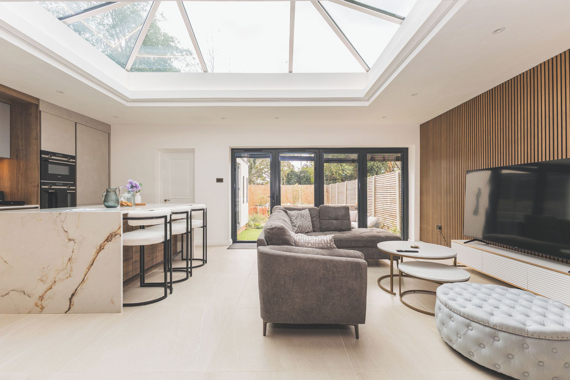 A modern living room with a skylight, a kitchen with a marble countertop, and a large TV.