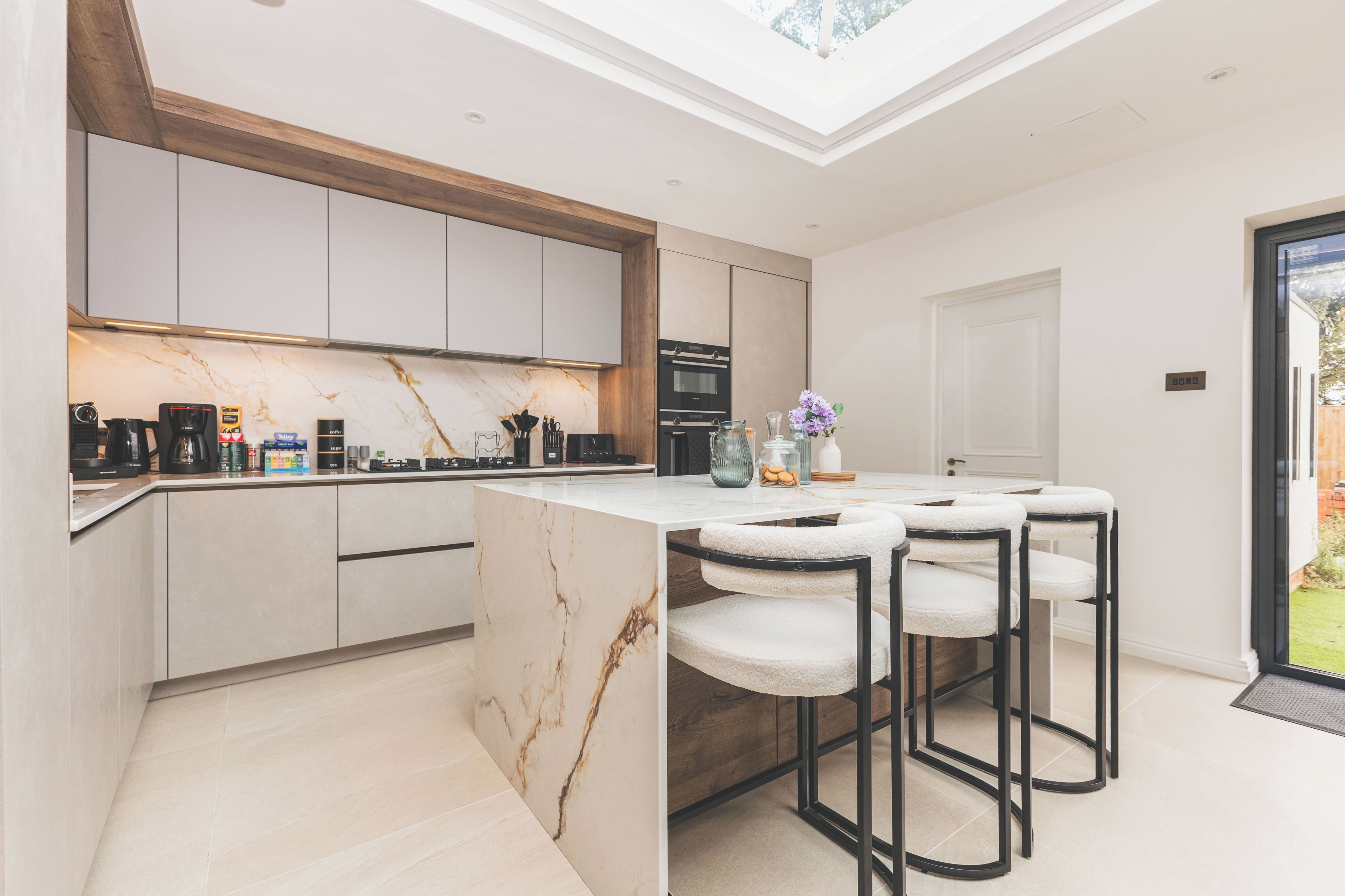 A modern kitchen with marble countertops, a central island with bar stools, and a skylight above.