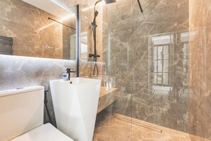 Ein modernes Badezimmer mit einer gläsernen Duschkabine, einem weißen Waschbecken und einer marmorverkleideten Wand.