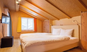 A bedroom with a large bed, a bedside table, a window with curtains, and wooden walls. - BEAUTIFUL ZERMATT ATTIKA APARTMENT WITH BALCONY & MOUNTAIN VIEWS (Zermatt)