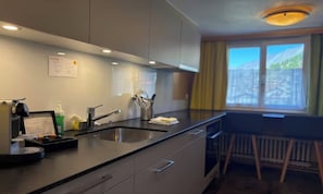 A modern kitchen with a built-in sink, a small dining area with a table and chairs, and a window with a mountain view. - BEAUTIFUL ZERMATT ATTIKA APARTMENT WITH BALCONY & MOUNTAIN VIEWS (Zermatt)