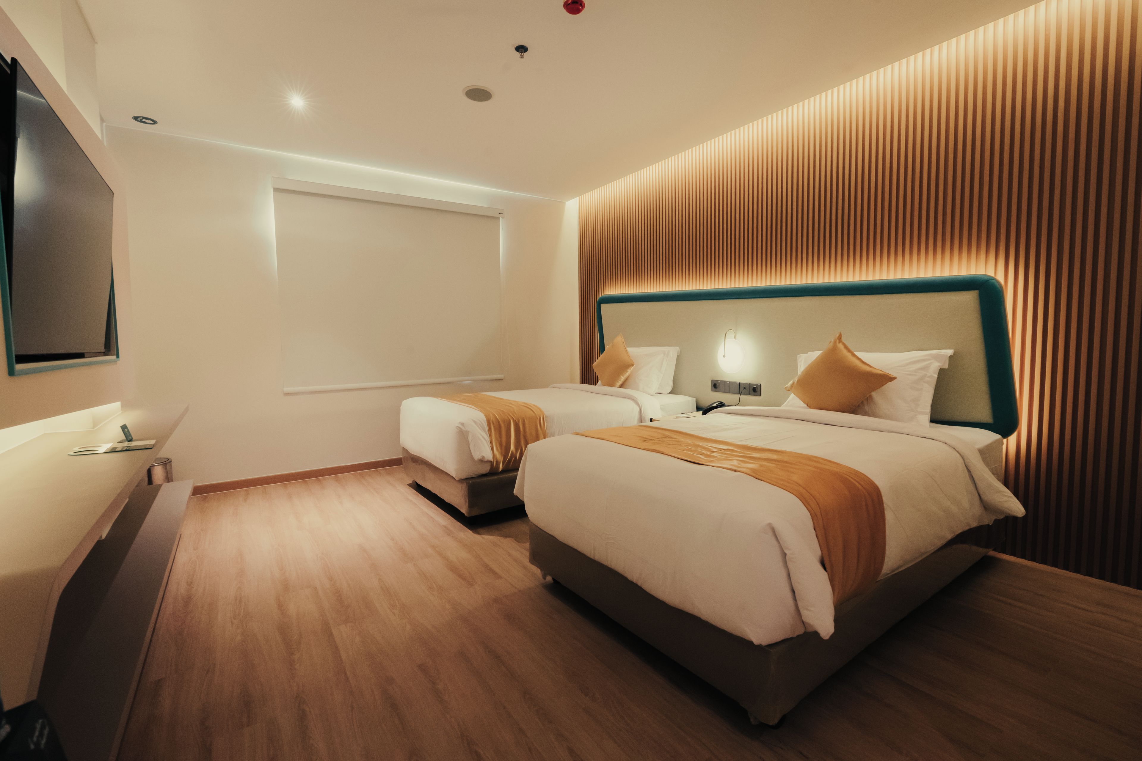 A modern hotel room with two beds, a flat-screen TV, and a wooden floor.