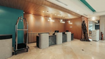 Un área de recepción con un revestimiento de panel de madera, un mostrador de recepción, un carrito metálico y un piso de mármol.