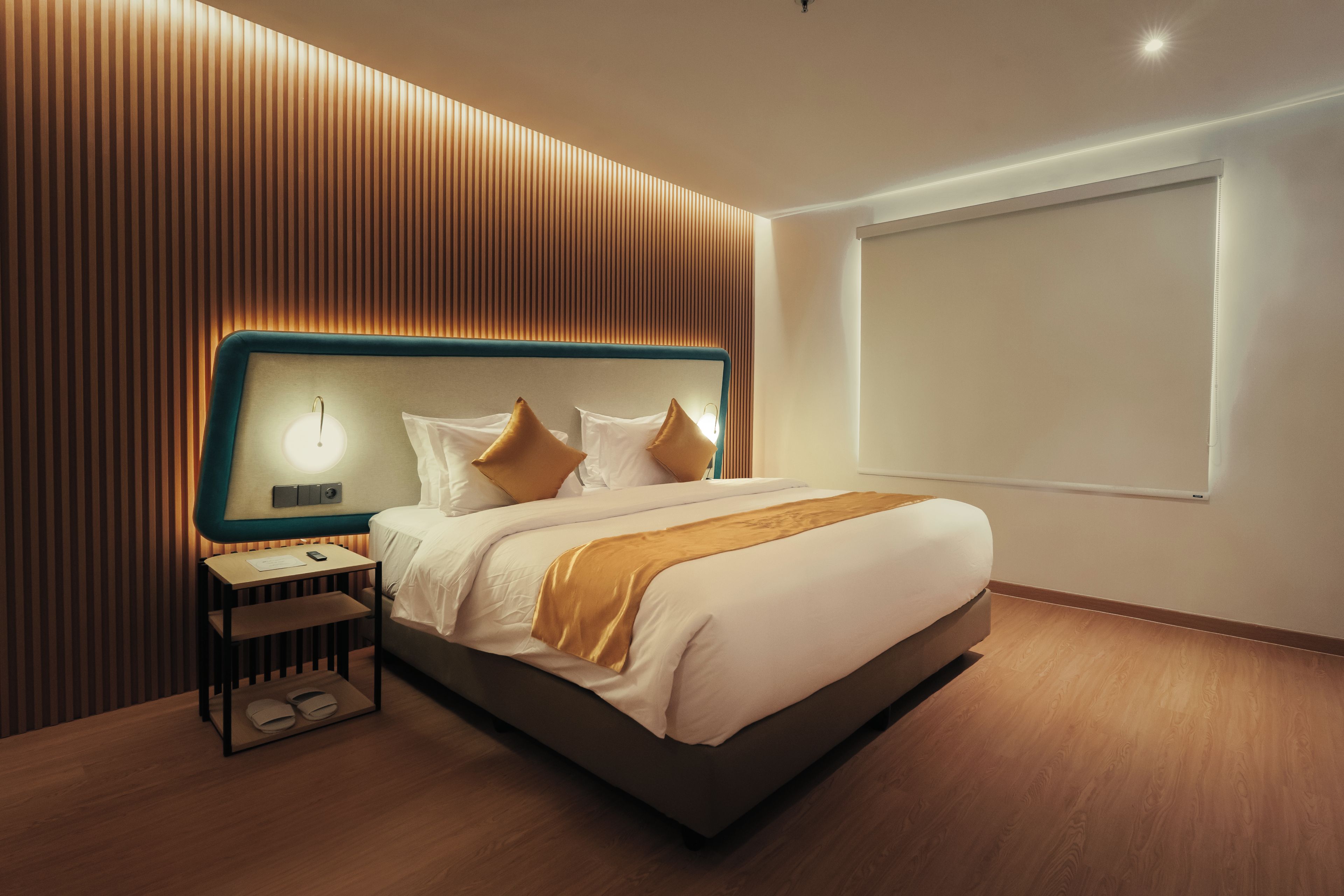 Una habitación de hotel moderna con una cama grande, una mesita de noche con lámpara y un ventanal amplio.