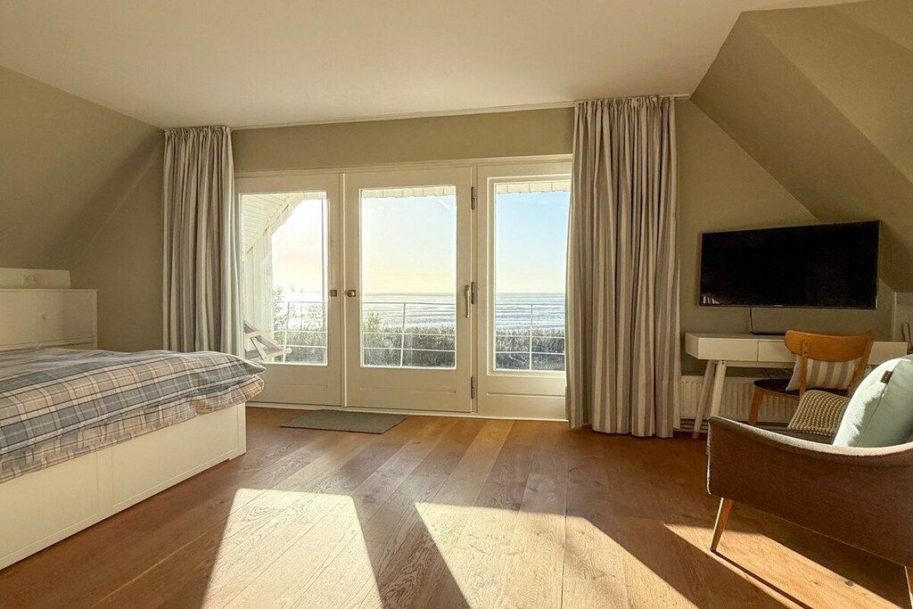 Un dormitorio con cama, escritorio, silla, televisor y balcón con cortinas.
