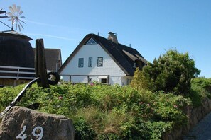 A white house with a black roof, a windmill, and a stone with the number 49. - Thatched house on the beach (Wyk auf Föhr)