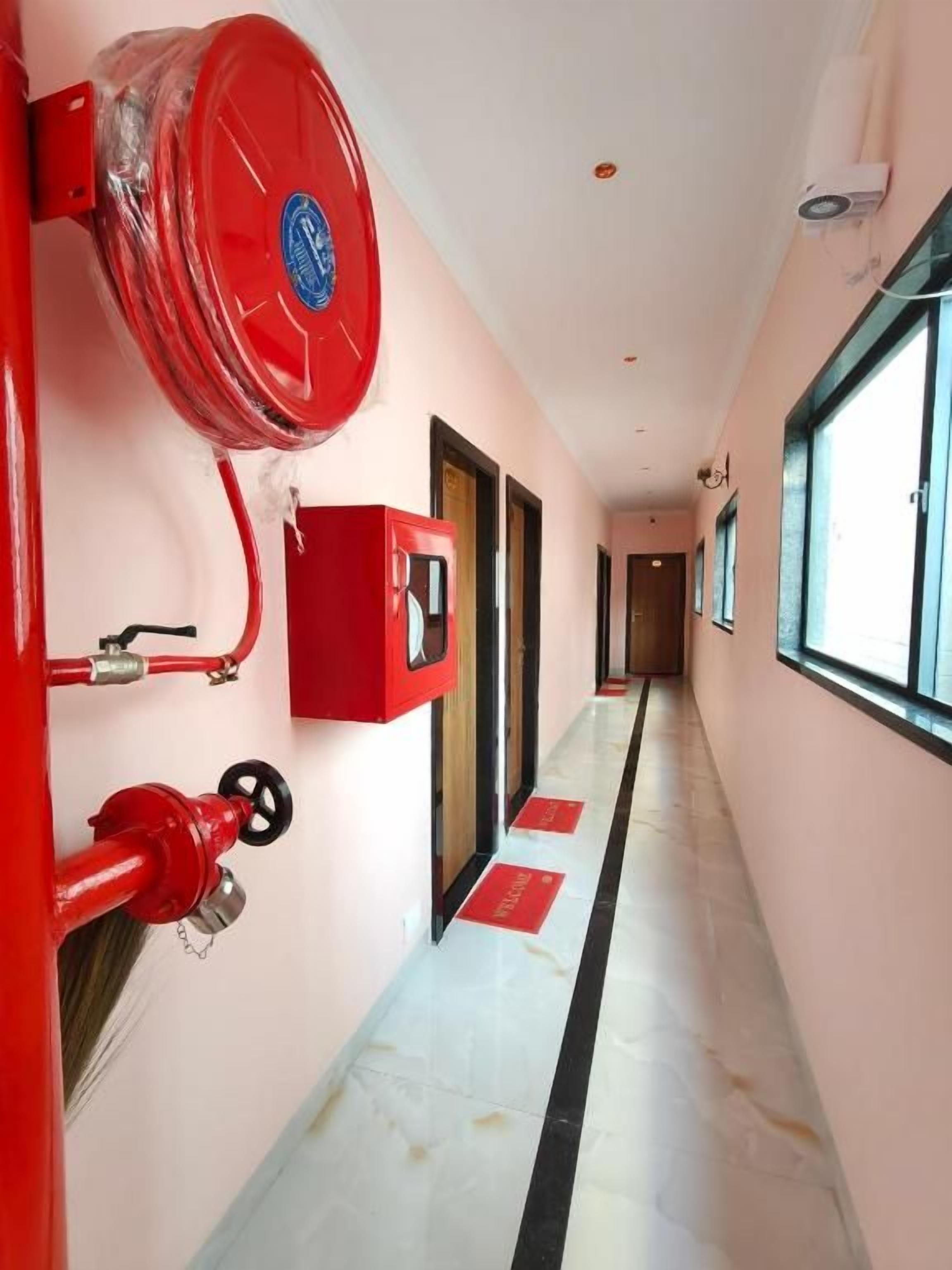 A hallway with a fire hose reel, a red fire alarm box, and a window on the right.