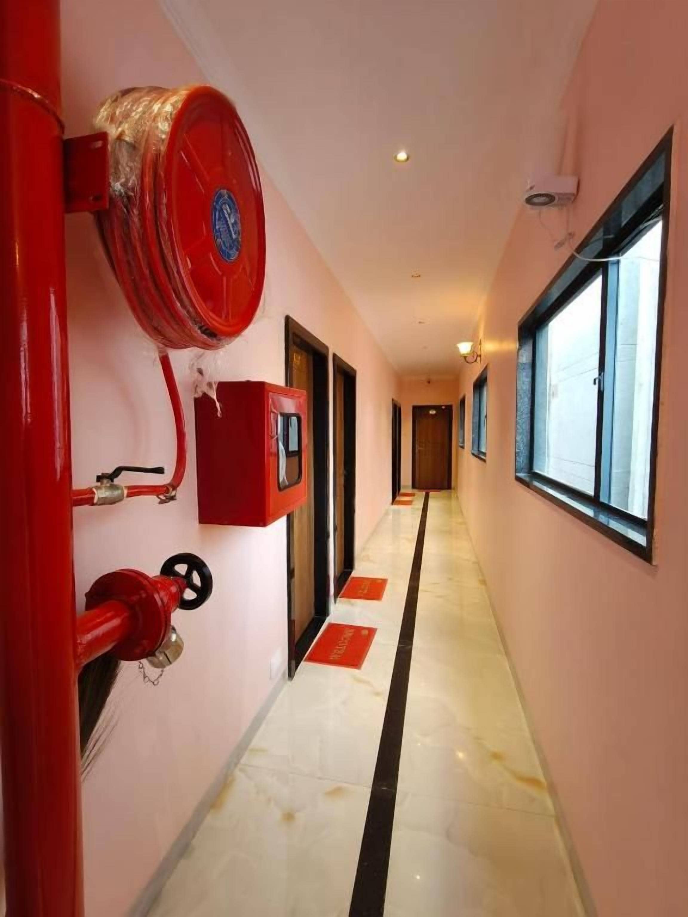 Un pasillo con un hidrante, un detector de incendios rojo y una puerta al final.
