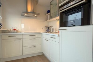A modern kitchen with white cabinetry, a built-in oven, and a Siemens brand microwave. - Holiday apartment with 1 bedroom (Wyk auf Föhr)