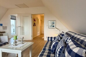 Ein Zimmer mit einem karierten Sofa, einem Glastisch mit Kerzen und einer Tür zu einem weiteren Raum.