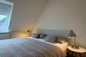 Ein Schlafzimmer mit einem Bett, Kissen, einem Nachttisch mit Lampe und einem Fenster.