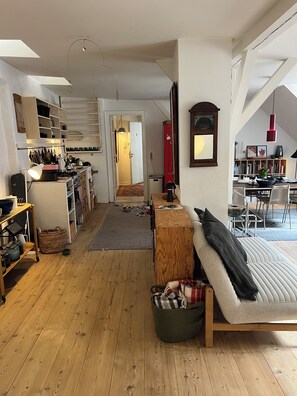 A spacious living area with a sofa, a dining table, and a kitchen area with wooden cabinets and a red refrigerator. - Bohemian rooftop flat with shared terrace in the heart of pictoresque Nyhavn (København)