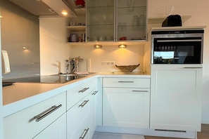 A modern kitchen with white cabinetry, a built-in oven, and a microwave. - Holiday apartment with 1 bedroom (Wyk auf Föhr)