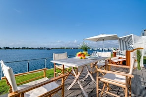 An outdoor dining area with a view of the water, a table with chairs, and a fruit bowl. - Holiday apartment with 2 bedrooms (Kappeln, Ostseeresort Olpenitz)