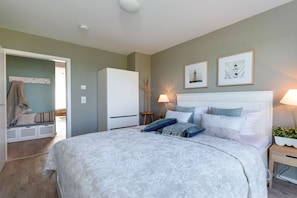 A bedroom with a large bed, a wardrobe, a bedside table with a lamp, and a wall-mounted shelf. - Holiday apartment with 2 bedrooms (Kappeln, Ostseeresort Olpenitz)
