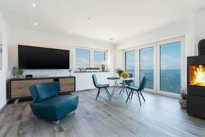 Ein modernes Wohnzimmer mit Flachbildfernseher, Kamin und Essbereich mit Meerblick.