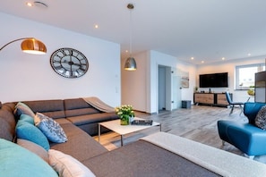 Ein modernes Wohnzimmer mit einem Ecksofa, einem Couchtisch und einem Fernseher im Hintergrund.