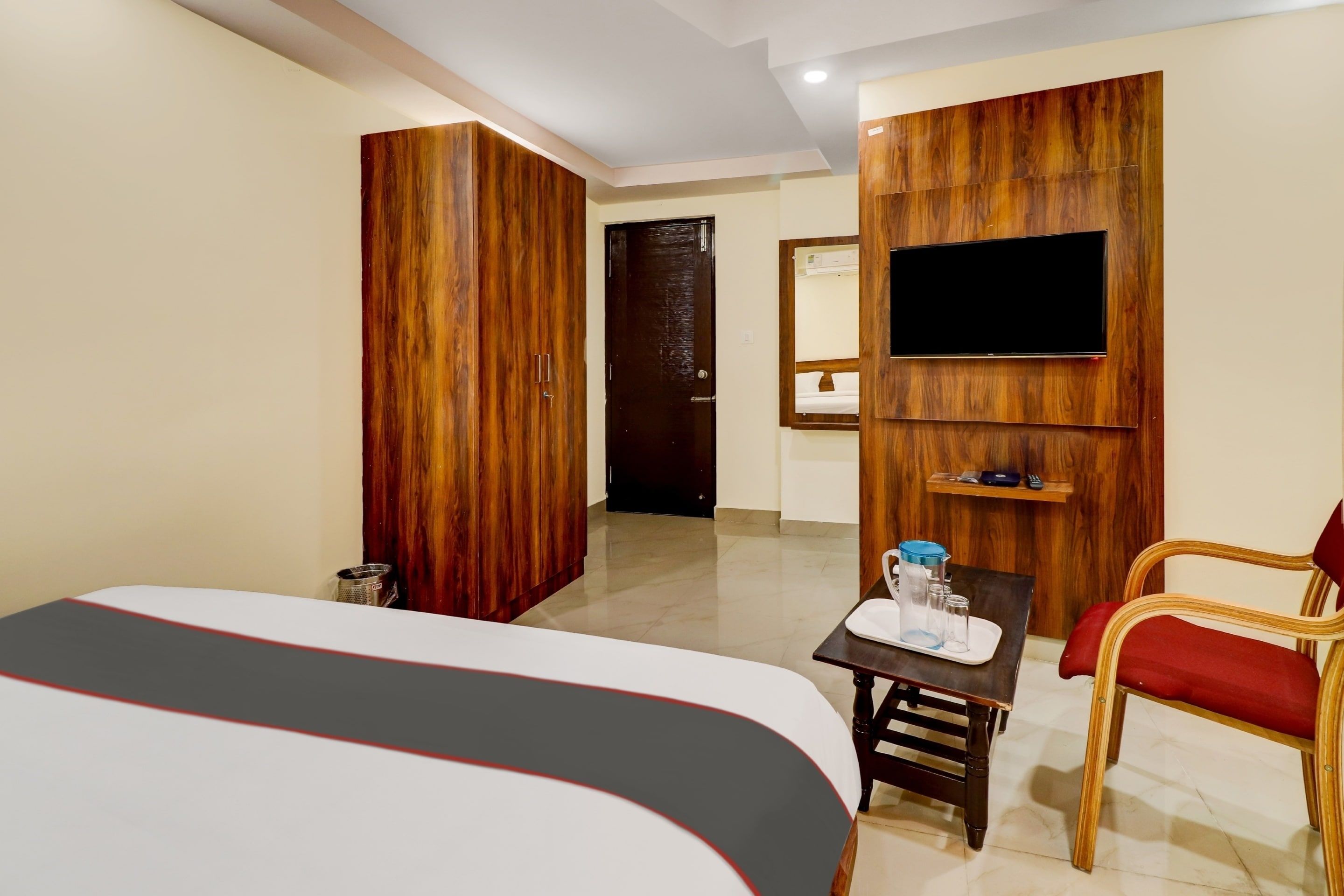 A hotel room with a bed, a desk with a chair, a television mounted on the wall, and a wooden wardrobe.