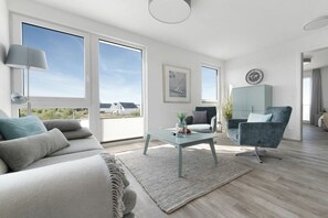 A modern living room with a sofa, armchair, coffee table, and large windows offering a view. - Apartment in Kappeln with swimming pool (Kappeln)