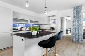 Una cocina moderna con armarios blancos, una isla central con taburetes y una planta en maceta.