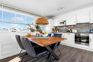 A modern kitchen with white cabinets, a wooden dining table, and a large window. - Holiday apartment with 1 bedroom (Olpenitz)