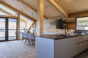 A modern kitchen with a large island, wooden beams, and a large window. - Superior Chalet # 5 with Sauna & Hot Tub (Turrach)