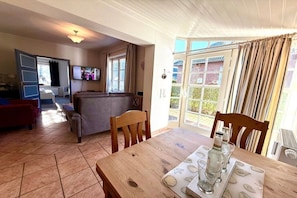 A cozy living area with a sofa, a wooden dining table with a placemat, and a television mounted on the wall. - House 94 - Apt. Ground Floor (Oldsum)