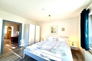 A hotel room with a bed, bedside tables, a wardrobe, and a window with curtains. - House 94 - Apt. Ground Floor (Oldsum)