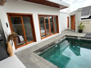 A modern house with a swimming pool, wooden sliding doors, and a stone exterior. - Peony Villa Lovina Private Pool (Sukasada)