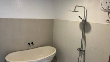 Un baño con una bañera independiente, un cabezal de ducha y un grifo de pared.