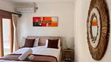 A hotel room with a bed, a wall-mounted air conditioner, a painting, a decorative mirror, and a window with curtains.