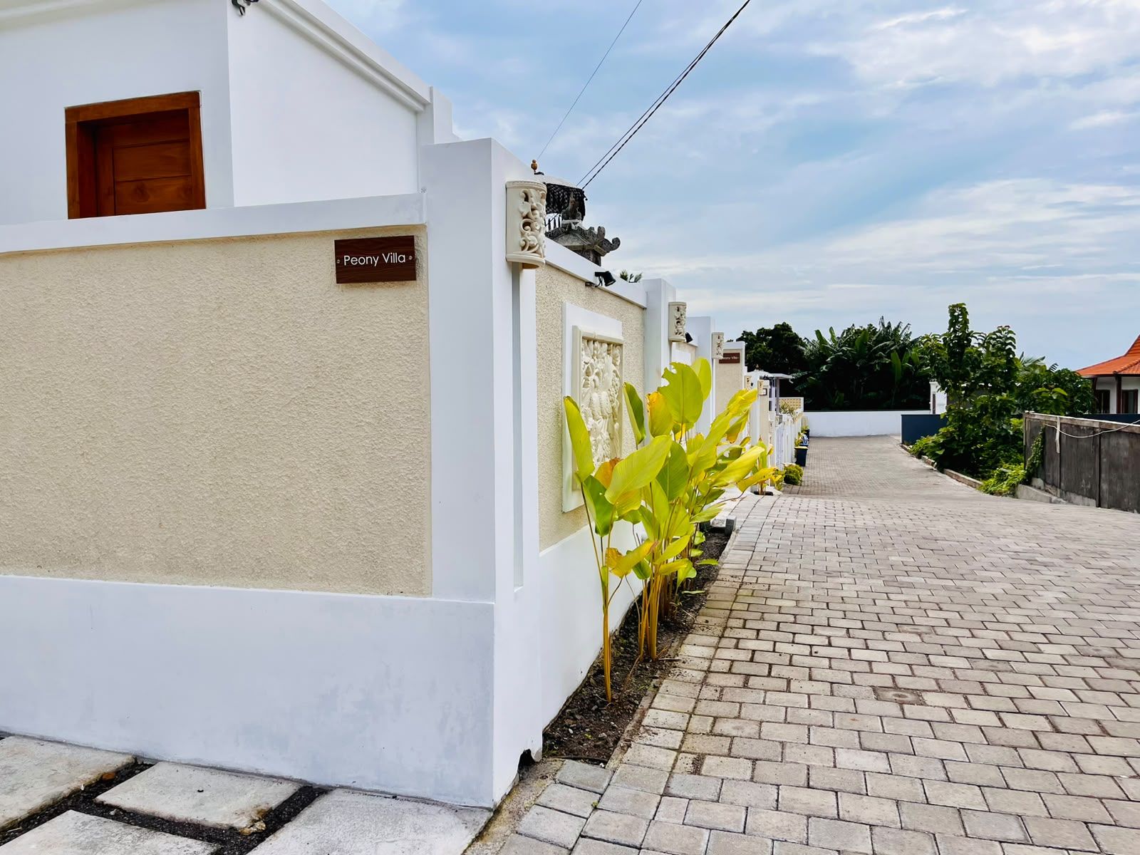Una villa blanca con camino de entrada pavimentado y un pequeño jardín.