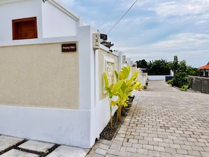 A white villa with a paved driveway and a small garden area. - Peony Villa Lovina Private Pool (Sukasada)