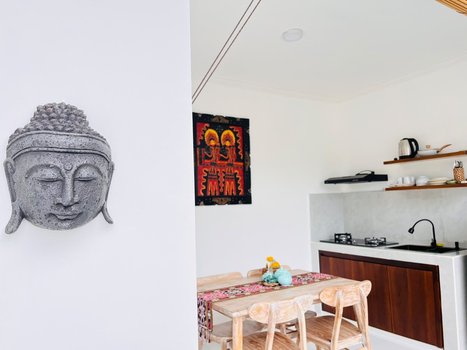 Een moderne keuken met een eethoek, met een Boeddha-beeld, een kleurrijk poster en een houten tafel met stoelen.