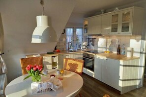 Une cuisine moderne avec des meubles blancs, un îlot central et un coin repas avec une table dressée pour deux personnes.