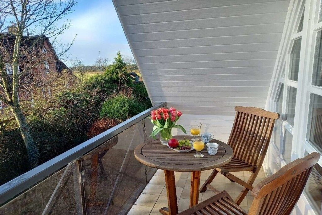 A balcony with a table set for two, a chair, and a vase of flowers.
