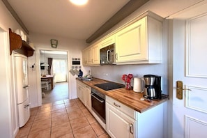 A kitchen with white cabinets, a wooden countertop, and a coffee maker. - Deichhof Apt. Möwennest (Dunsum)