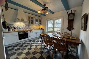 A kitchen with checkered flooring, white cabinets, a wooden dining table with chairs, a chandelier, and a wall-mounted clock. - Det Danske Hus - Apartment Starboard (Dunsum)
