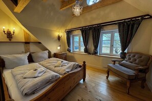 A bedroom with a wooden bed, a bench, a chandelier, and a window with curtains. - Det Danske Hus - Apartment Upper Deck (Dunsum)
