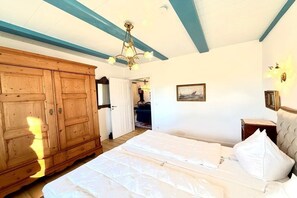 Ein Schlafzimmer mit großem Holzschrank, einem Bett mit weißer Bettwäsche, einer Pendelleuchte und einem gerahmten Bild an der Wand.